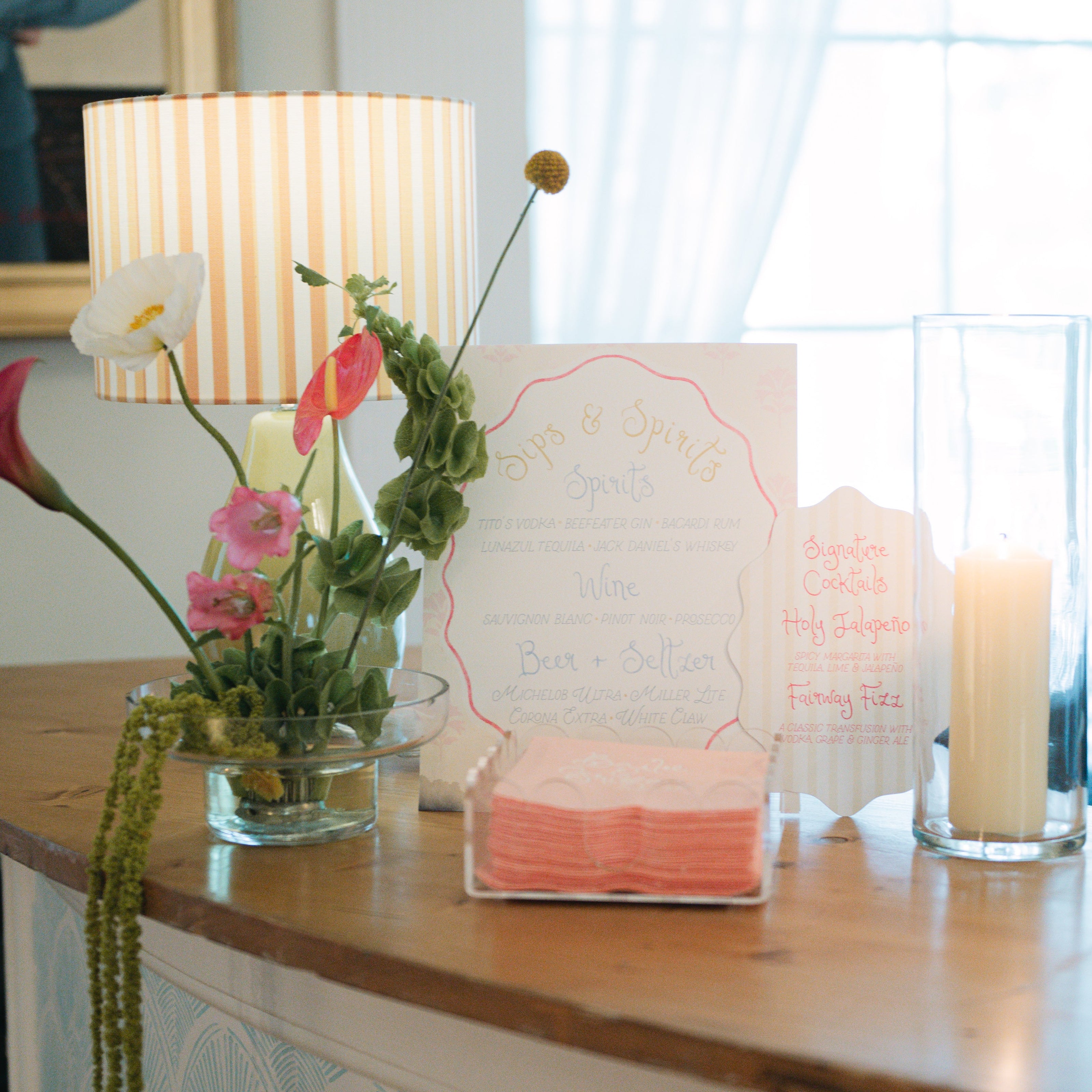 Custom wedding bar sign and signature cocktail sign displayed with personalized cocktail napkins, candles, and floral décor at a wedding reception.