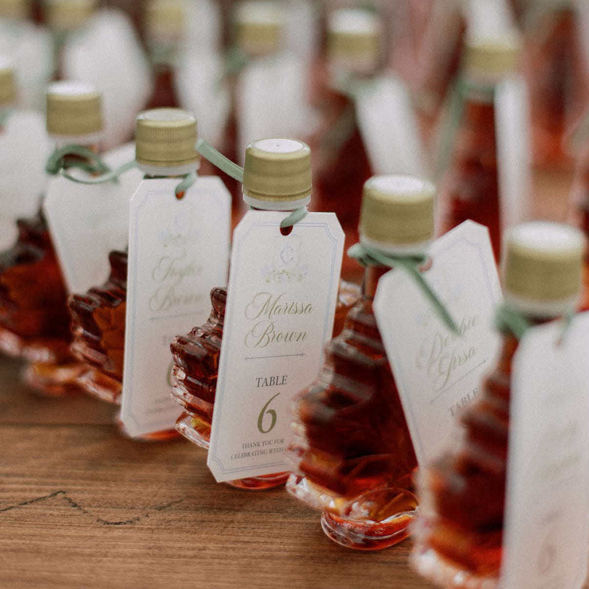 Custom designed favor tags on mini maple syrup bottles serving as the wedding seating chart/escort cards.