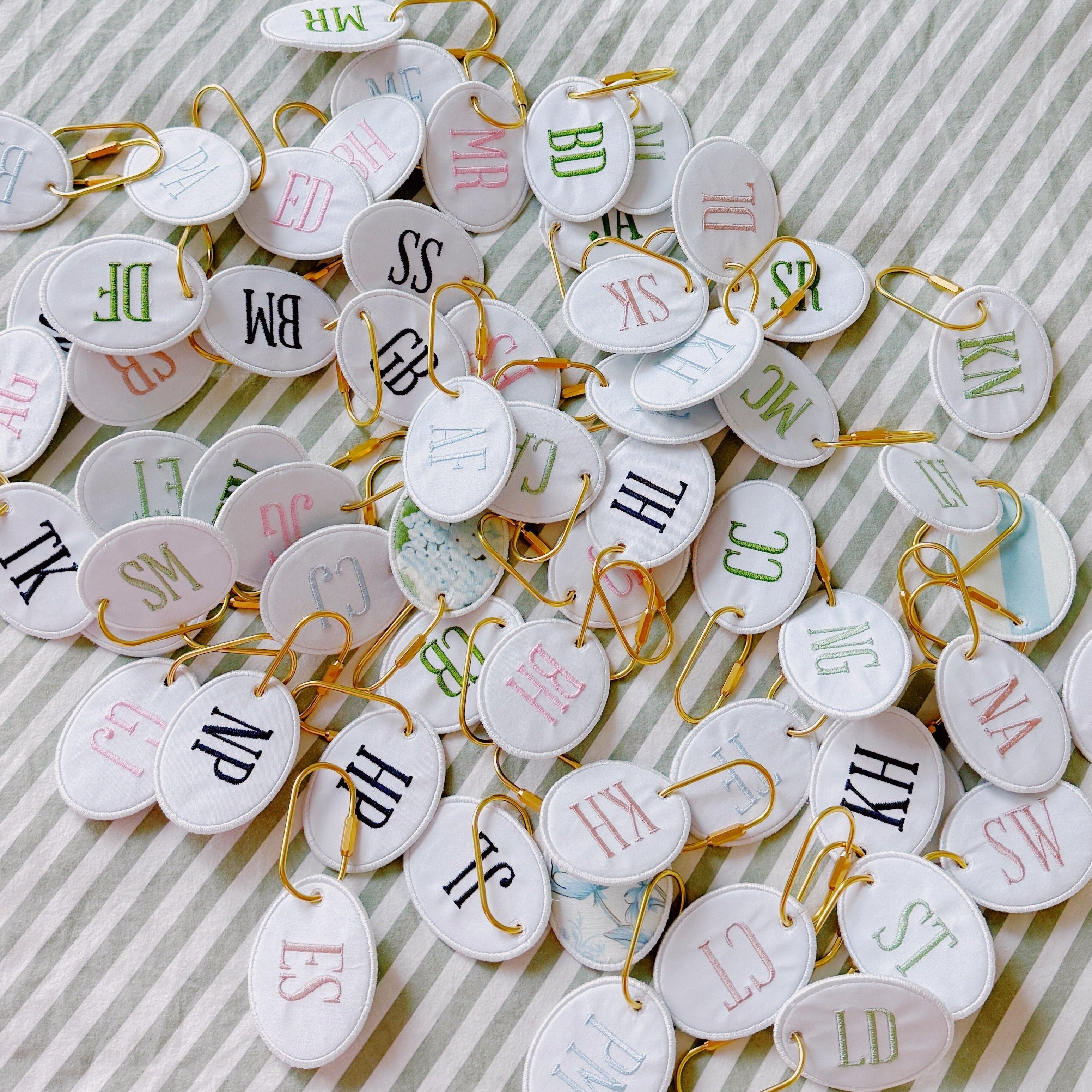 Collection of personalized embroidered bag charms featuring custom monograms on oval fabric keychains with gold hardware