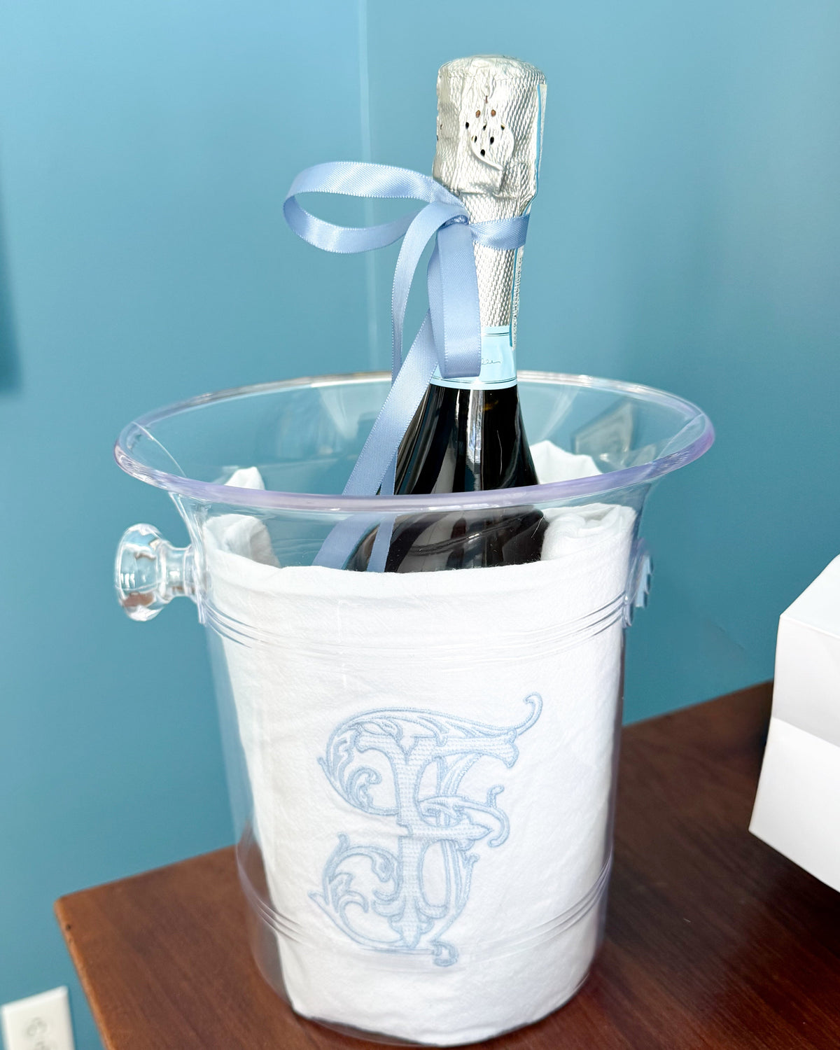 Personalized embroidered tea towel with an elegant custom monogram, styled in a champagne bucket with a bottle of champagne for gifting and entertaining.